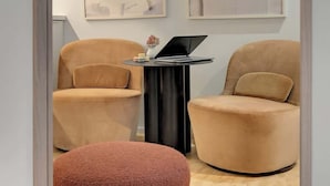 Ein Zimmer mit zwei Sesseln, einem kleinen schwarzen Beistelltisch mit einem Laptop und einem Spiegel, der das Zimmerinnere reflektiert.