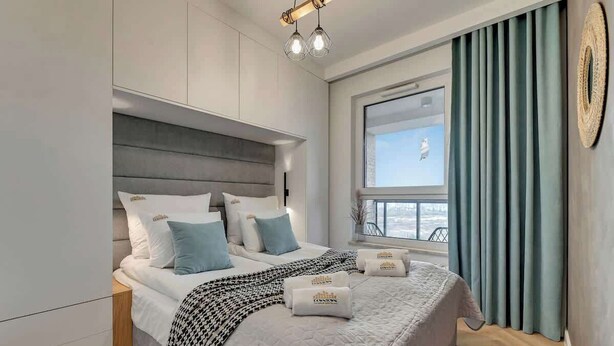 Ein modernes Hotelzimmer mit einem großen Bett, einem Fenster mit Vorhängen und Blick auf die Stadt.