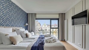 A modern hotel room with a bed, a TV, and a view of buildings. - Rezydencja Wintera Grande | River View (Gdańsk)