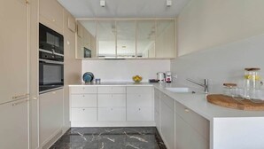 A modern kitchen with a built-in oven, a large mirror above the sink, and a marble floor. - Rezydencja Wintera Grande | River View (Gdańsk)