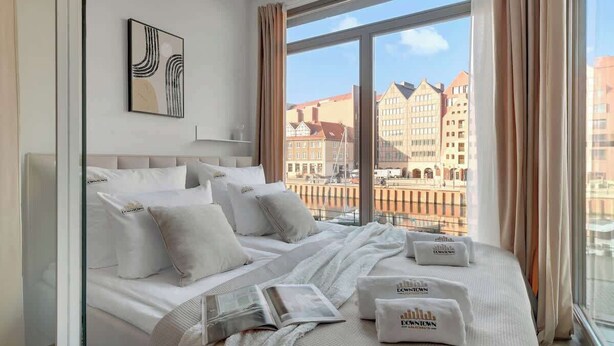 Hotellihuone, jossa on suuri sänky, näköala kaupunkiin ja seinällä oleva taideteos, joka on kehystetty.