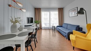 Ein modernes Wohnzimmer mit Essbereich, einer Couch, einem gelben Sessel und einem Fernseher.