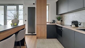 A modern kitchen with a central island, dark cabinetry, and a view of the city. - Żurawie B127A | Shipyard | Foodhall Montownia (Gdańsk)
