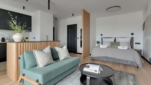 A modern hotel room with a sofa, a round coffee table, a bed with a grey duvet, and a wooden partition. - Żurawie B127A | Shipyard | Foodhall Montownia (Gdańsk)