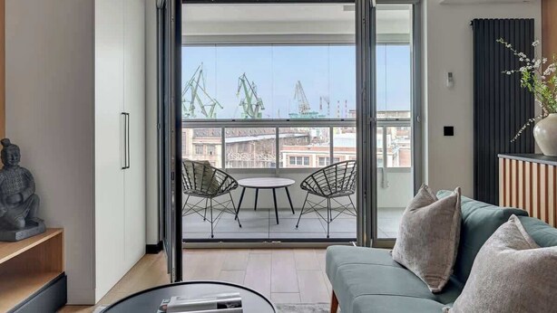A modern living room with a sliding glass door leading to a balcony with a view of cranes. - Żurawie B127A | Shipyard | Foodhall Montownia (Gdańsk)