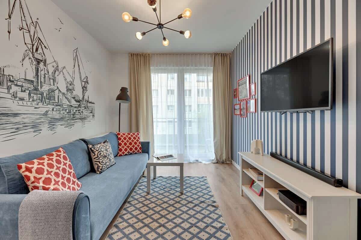 Una sala de estar moderna con sofá, mesa de centro, televisor, pared a rayas y un ventanal grande.
