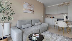 Ein modernes Wohnzimmer mit einem grauen Sofa, einem runden Couchtisch und einem Essbereich mit einem weißen Tisch und Stühlen.