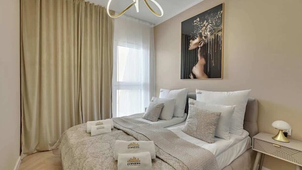 Ein Hotelzimmer mit Bett, Nachttisch, einem Fenster mit Vorhängen und einem Gemälde an der Wand.
