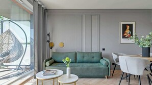 En moderne stue med en grøn sofa, to runde borde, et spiseområde med stole, en hængestol og et indrammet kunstværk på væggen.