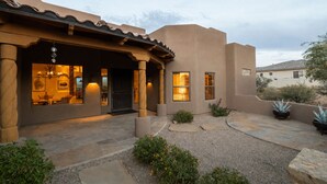 A stucco building with a covered patio, a dining area with a table and chairs, and a small garden with plants and a birdbath. - Infinity Pool, Mountain Views and Putting Green (Scottsdale)