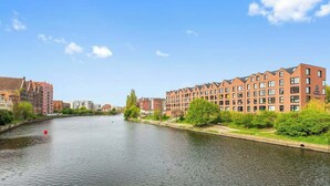 A river with buildings on both sides, including a red-brick building with multiple windows and a modern building with a flat roof. - Rezydencja Wintera 53 | Riverside (Gdańsk)
