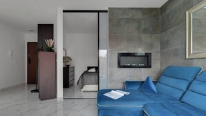 A modern living room with a blue sofa, a fireplace, and a glass door leading to another room. - Rezydencja Wintera 53 | Riverside (Gdańsk)