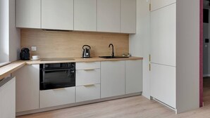 A modern kitchen with white cabinets, a wooden countertop, a coffee maker, a kettle, and a sink. - Nowa Letnica 5 | Seaside Apartament (Gdańsk)