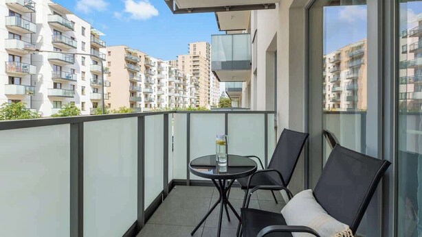 A balcony with a glass balustrade, a round table with a chair, and a cushion. - Nowa Letnica 5 | Seaside Apartament (Gdańsk)