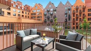 Een balkon met rieten meubilair, een tafel met een tijdschrift en uitzicht op meerlaags gebouwen.