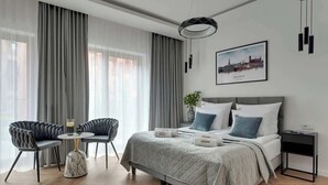 Een moderne hotelkamer met een bed, twee fauteuils, een bijzettafeltje en een stadsgezichtschilderij aan de muur.