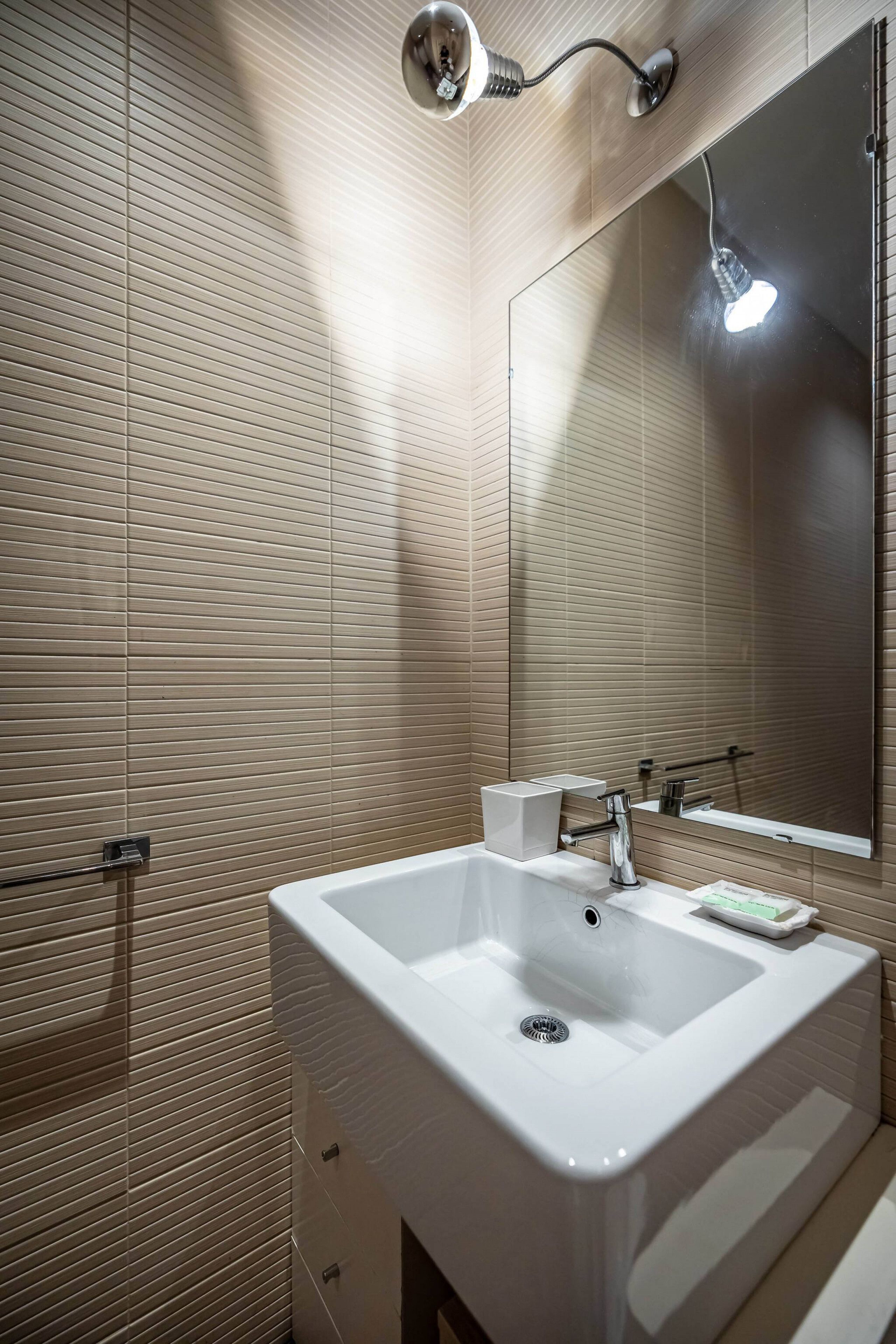 Une salle de bain avec un grand miroir, un lavabo blanc, une serviette et un luminaire.