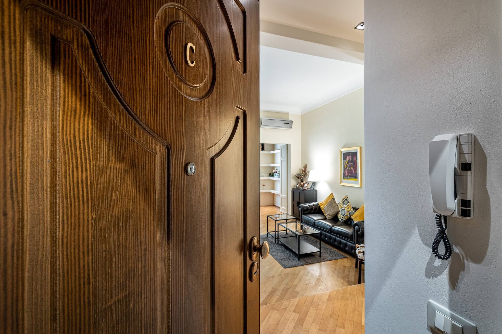 A wooden door with a circular emblem, a living room with a sofa and a coffee table, and a wall-mounted phone.