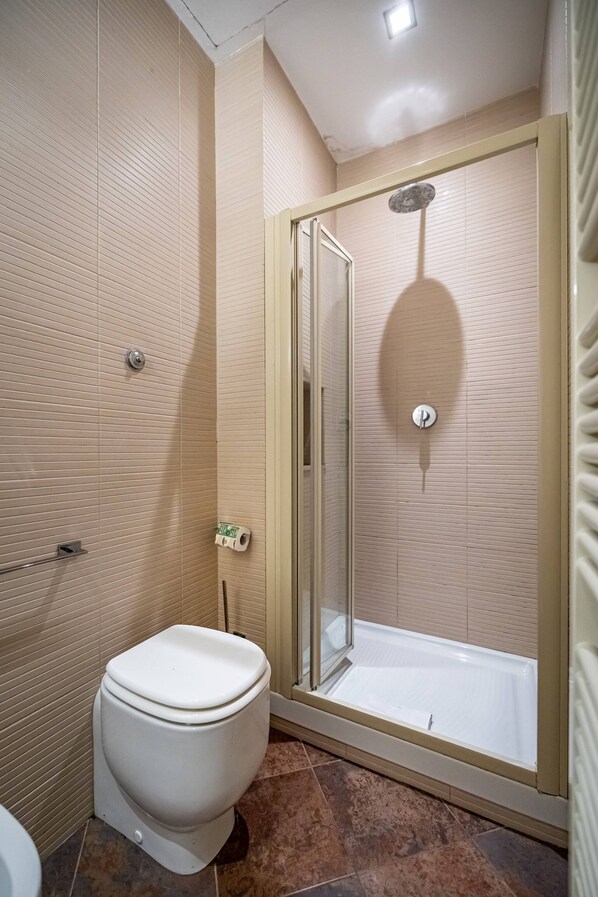 A bathroom with a toilet, a shower with a glass door, and tiled walls. - Servi A (Florence)
