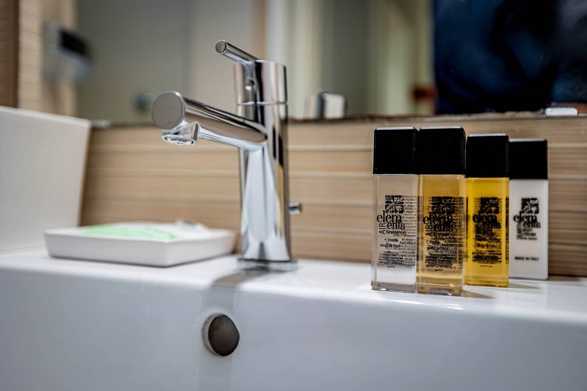 A bathroom sink with a chrome faucet, a soap dispenser, and three bottles of Elemis shampoo.