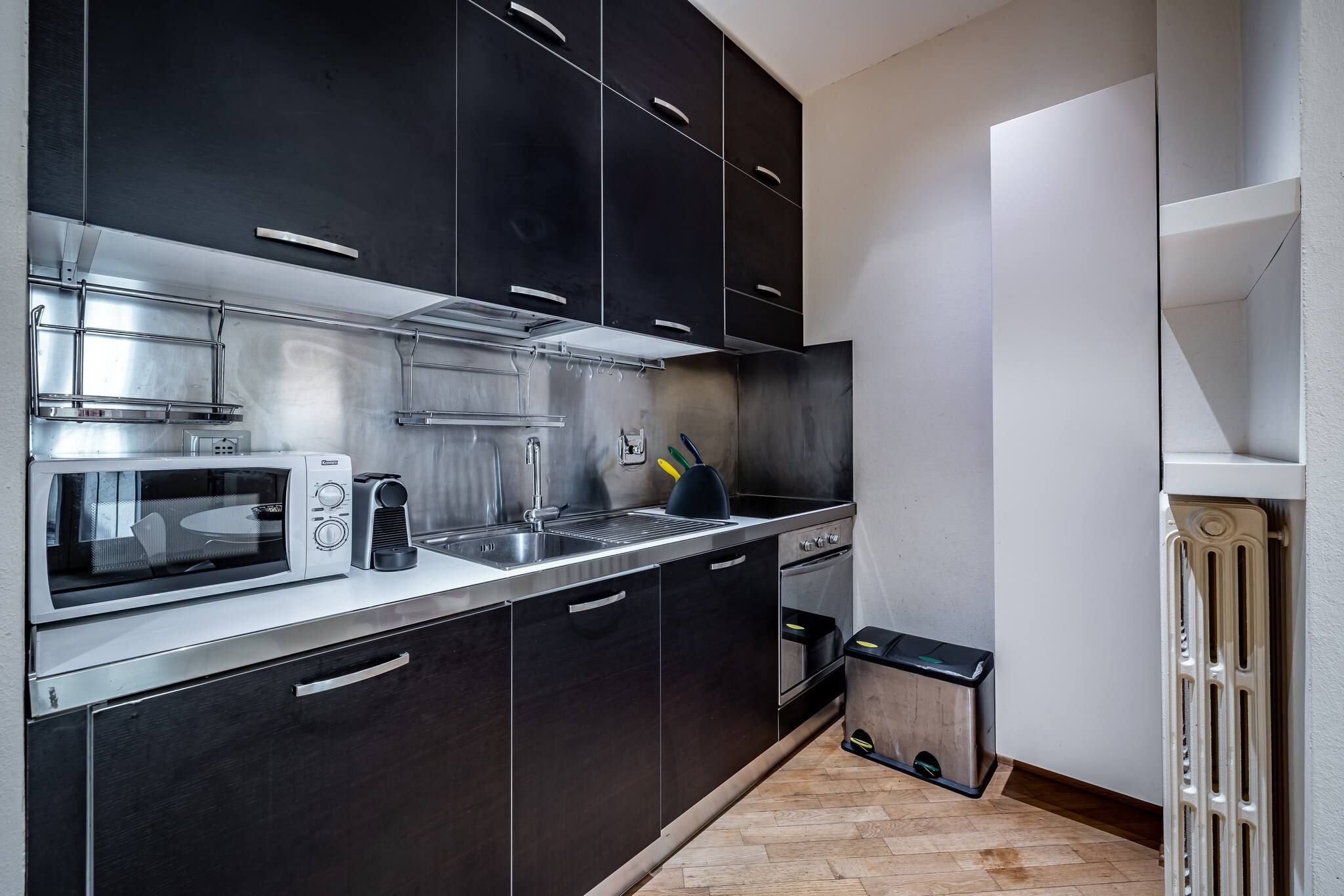 Una cocina moderna con electrodomésticos de acero inoxidable, armarios oscuros y un pequeño cubo de basura.