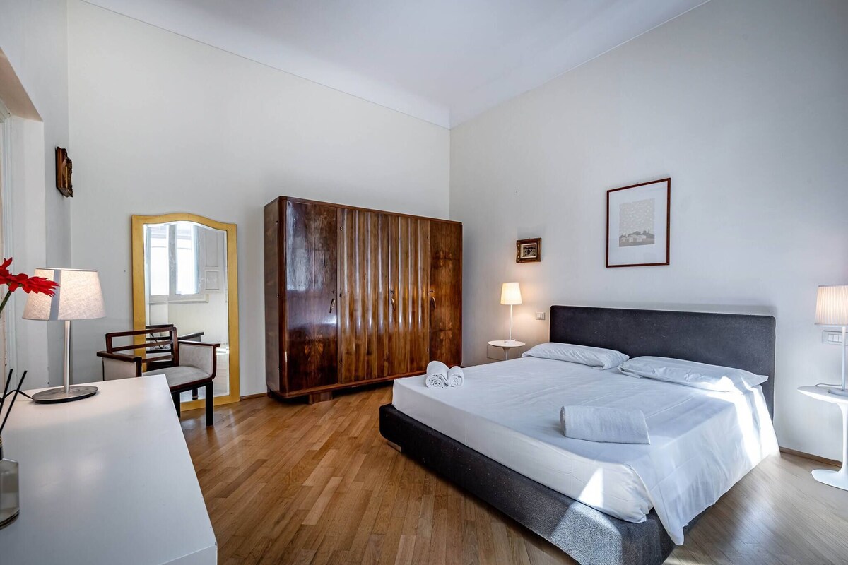 Une chambre à coucher moderne avec un grand lit, une armoire en bois, un bureau avec une lampe et une chaise.