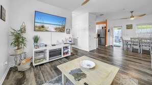 Ein geräumiges Wohnzimmer mit Holzboden, Deckenventilator, Esstisch und einer Küche im Hintergrund.