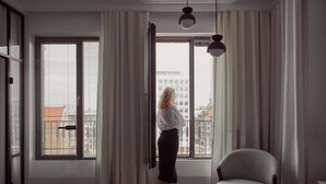 Une pièce avec une grande fenêtre, une chaise et une personne debout près de la fenêtre.