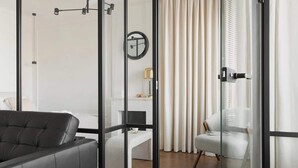 Une pièce moderne avec un canapé en cuir noir, un bureau blanc, une chaise et une cloison en verre.