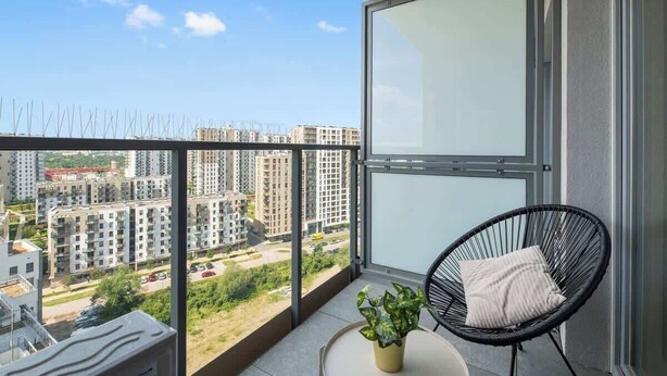 A balcony with a view of high-rise buildings, a potted plant, and a black chair with a cushion. - Nowa Letnica 152 | Seaside Deluxe Apartament (Gdańsk)
