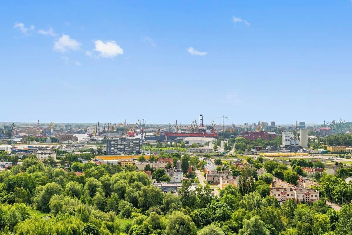 Un paisaje urbano con edificios industriales, grúas y una combinación de construcciones residenciales y comerciales.