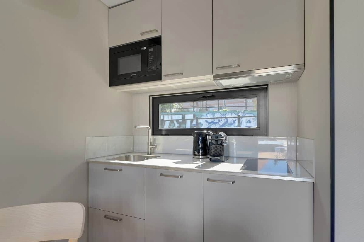 A compact kitchenette with a microwave, a coffee maker, and a window above the sink.