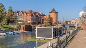 A riverside view with historic buildings, a tower, and a modern structure by the water.