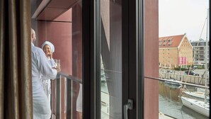 A balcony with a view of a canal and boats, a building with a red roof, and a person holding a glass. - Hi Stay Red Velvet & Gold | Unique View (Gdańsk)