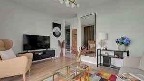 Ein modernes Wohnzimmer mit Fernseher, beiger Couch, Glastisch und farbenfrohem Teppich.