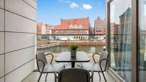 A balcony with a table and chairs, a potted plant, and a view of a river with buildings in the background. - Waterlane E3A | Spa, Pool & Gym | River View (Gdańsk)