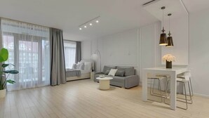 A modern living room with a sofa, a coffee table, and a dining area with chairs. - Waterlane E3A | Spa, Pool & Gym | River View (Gdańsk)