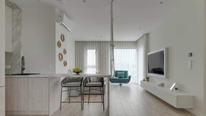 Una cuina moderna amb un respatller de marbre, zona de menjador amb dues cadires, un sofà color turquesa, un televisor penjat a la paret i una finestra gran amb cortines.