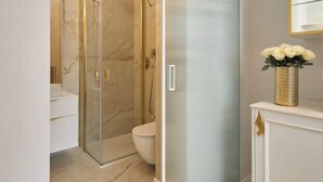 Un baño moderno con cabina de ducha de vidrio, inodoro y tocador con un jarrón dorado.