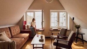 Ein gemütliches Schlafzimmer im Loft-Stil mit schräg versiegelter Decke, einem großen Fenster, einem braunen Ledersofa, einem Holztisch und einem kleinen Beistelltisch.