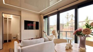 A modern living room with a flat-screen TV, a sofa, a dining table, and a vase with flowers.