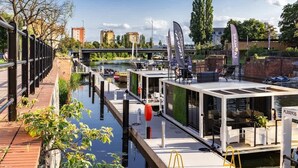 A floating restaurant with outdoor seating, a dock, and a view of a river and bridge.