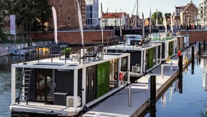A canal with floating homes docked, a historic tower, and a modern building with a glass facade.