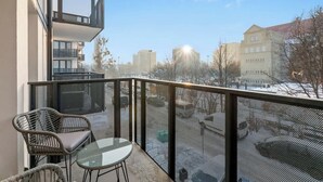 En balkon med et glastabel og stole, der kigger ud over en sneklædt gade og bygninger.