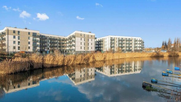 Et moderne boligkompleks med et roligt vandareal i forgrunden, der spejler bygningerne.