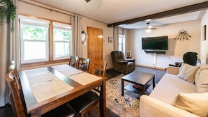 A living room with a sofa, a TV, a wooden dining table, and a ceiling fan.