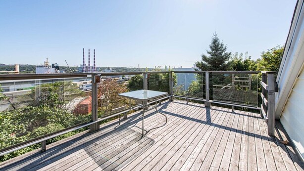 A wooden deck with a table and bench, overlooking a cityscape with industrial buildings and a river.