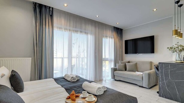 Ein modernes Hotelzimmer mit Bett, Sofa, Fernseher und Frühstückswagen.