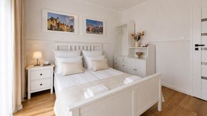 Um quarto com uma cama grande, uma mesa de cabeceira com luminária, cômoda e duas molduras na parede.