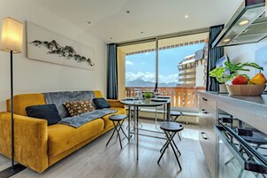Ein modernes Wohnzimmer mit einem gelben Sofa, einem Esstisch und einem Balkon mit Blick auf die Berge.